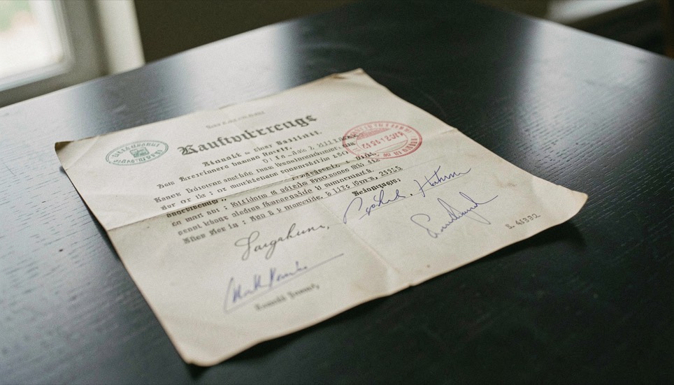 Ein alter Kaufvertrag mit Stempel, Siegellack und mehreren Unterschriften liegt auf einem dunklen Tisch.